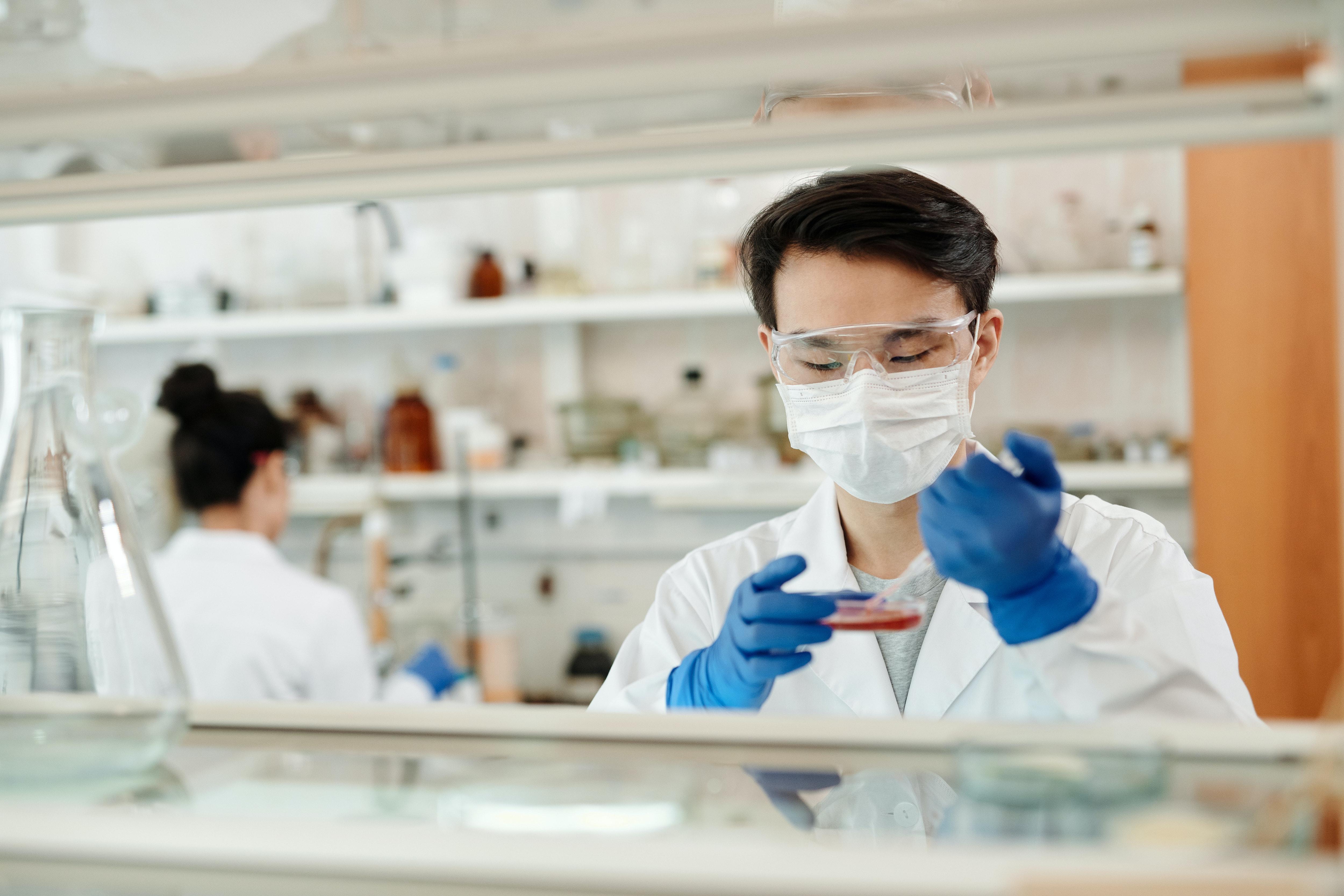 Young man works on a petri dish while a young woman works behind him